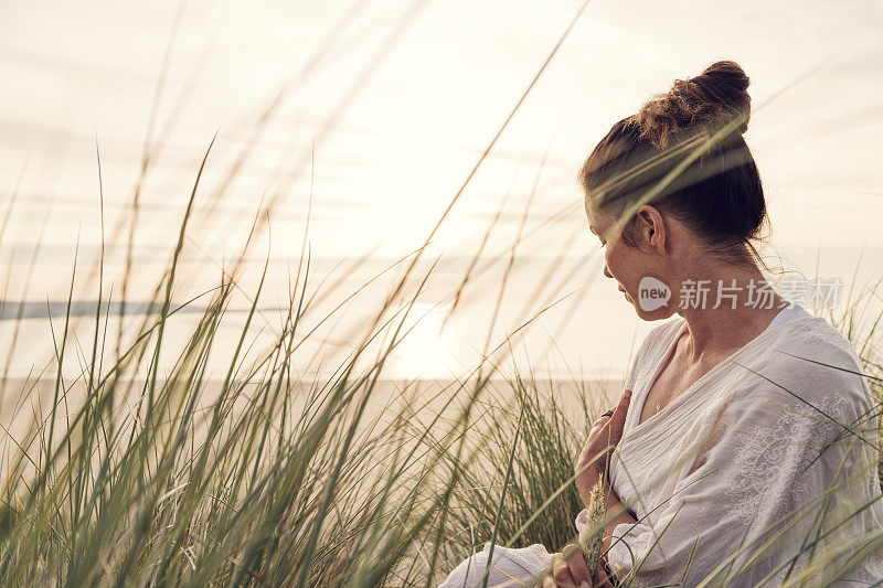一名女子坐在康沃尔Gwithian Towans海滩的沙丘上，享受着夏末的阳光。